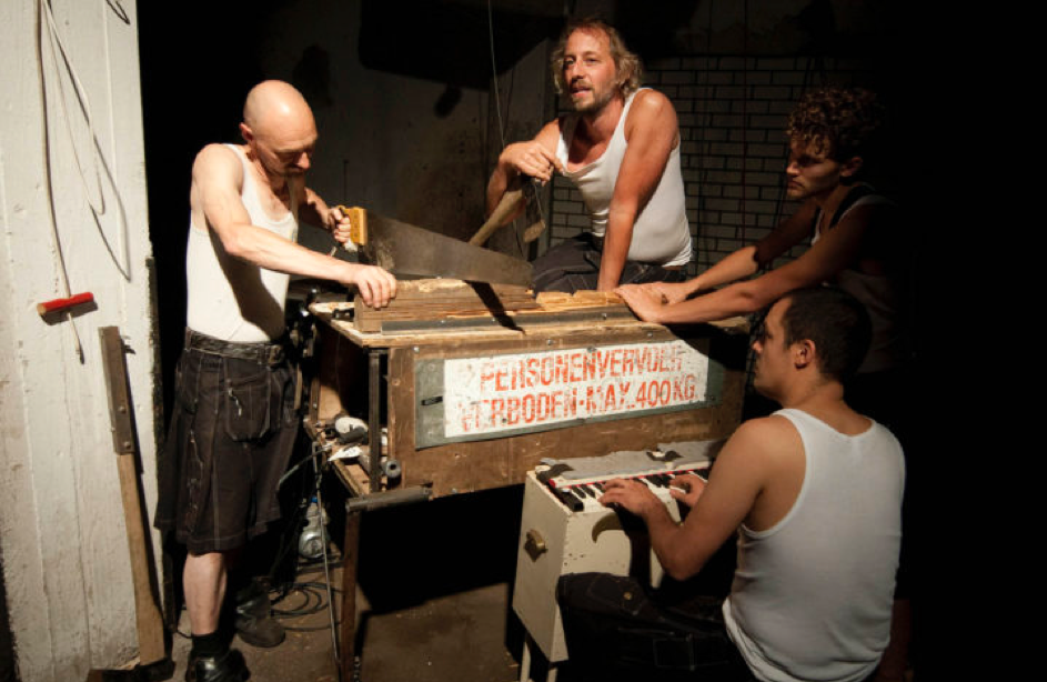 De leden van 'Wij zijn bot' in witte onderhemden rondom hun muziekinstrumenten voor hun voorstelling ' Het geluid van het museum'.